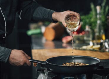 Kochen mit Wein: Mann gießt Weißwein in Pfanne