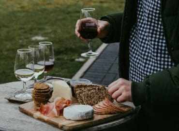 Snacks zum Wein: Person mit Rotwein in der Hand und einer Käseplatte vor sich