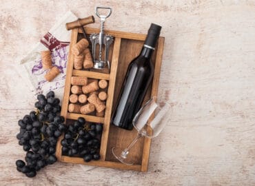 veganer Wein: Flasche Rotwein, Korken, Gläser und Korkenzieher in Holzschale