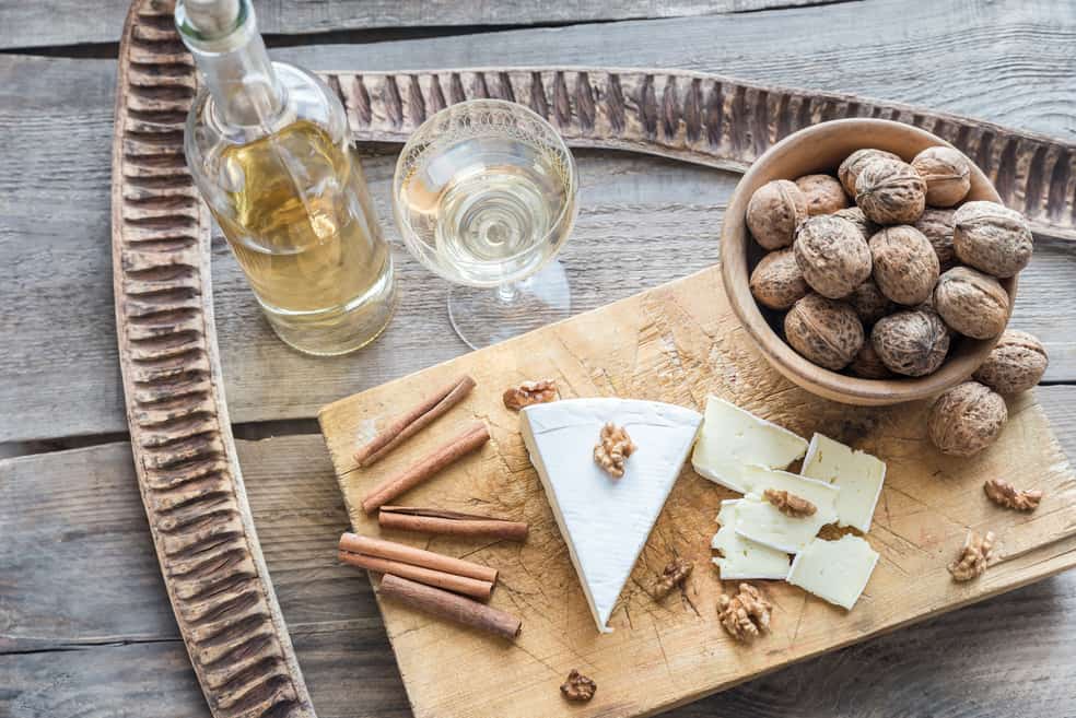 Käse mit Walnüssen und einem Glas Wein auf einem Holzbrett